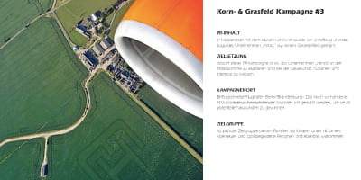 Blick aus einem Flugzeug auf eine Rasenfläche mit Minos‑Logo, Flugzeugmotor im Vordergrund.