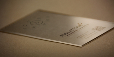 Transparente Visitenkarte aus Acrylglas mit einem aufgedruckten Kamera-Sucher im oberen Drittel. Im unteren Teil befinden sich das Augenzeuge-Logo, Adressdaten und ein QR-Code in schwarzer Schrift.