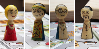 Vier handbemalte Holzfiguren – Partyboy, Öko/Hippie, Oma und Dame – stehen auf dem Spielbrett.