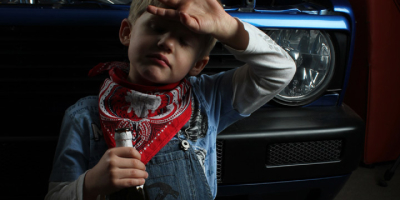 Ein humorvolles Motiv: Der Junge kniet erschöpft vor dem Auto und wischt sich mit dem Handrücken über die Stirn. In der anderen Hand hält er eine Flasche Bier (Berliner Kindl). Er imitiert die typische Geste eines Arbeiters nach getaner Arbeit.